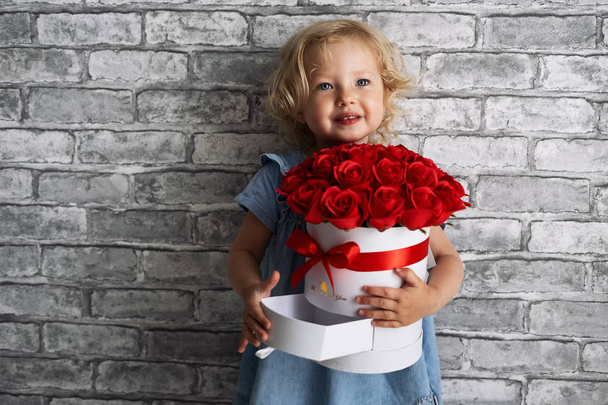 A little girl with a large bouquet of roses in a sick round white box. - Foto, Imagem