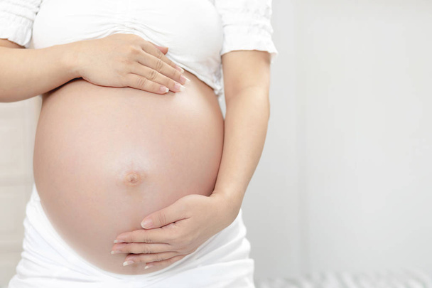 Nueva mamá Mujer embarazada en ropa interior blanca utiliza el tacto de la mano barriga con el bebé. Mujer joven esperando un bebé De pie al aire libre
. - Foto, imagen