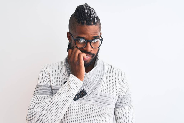 Homem afro-americano vestindo camisola cinza e óculos sobre fundo branco isolado olhando estressado e nervoso com as mãos na boca mordendo unhas. Problema de ansiedade
. - Foto, Imagem