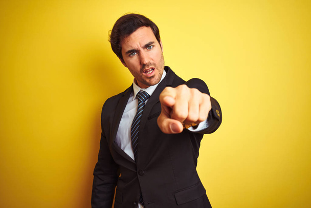 Jeune homme d'affaires beau portant costume et cravate debout sur fond jaune isolé pointant mécontent et frustré à la caméra, en colère et furieux contre vous
 - Photo, image