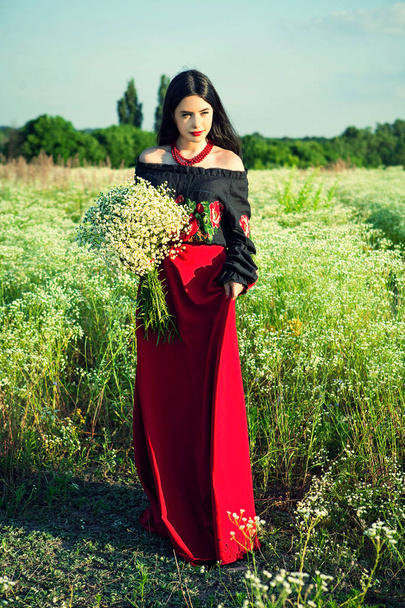 smiling young girl with a bouquet of flowers in the field, walk in the field, girl posing, girl smile, long hair, closed eyes, red beads, black hair, portrait of a girl, red lips, rite of passage, happy girl, sexy girl, bouquet of flowers in hands - Photo, Image