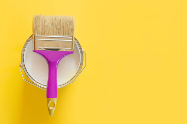 Purple brush with open can of white paint on yellow background.  - 写真・画像