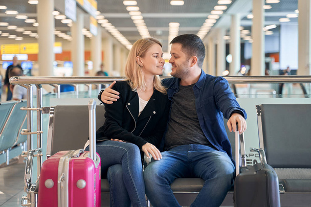 Image of happy woman and man in love sitting in waiting room at airport - Photo, Image