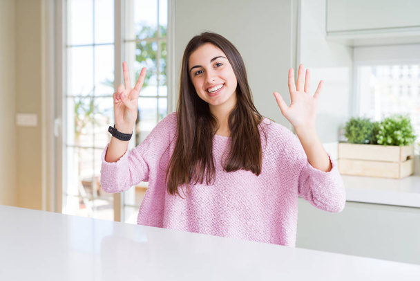 ピンクのセーターを着た美しい若い女性は、自信を持って幸せに微笑みながら、指番号7を示し、指で指を向けます. - 写真・画像