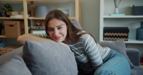 Slow motion portrait of charming woman looking at camera smiling sitting on sofa - Filmagem, Vídeo