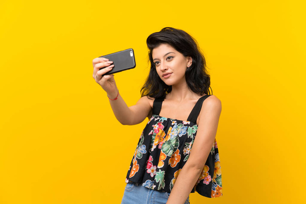 Młoda kobieta na białym tle żółty co selfie z telefonem komórkowym - Zdjęcie, obraz