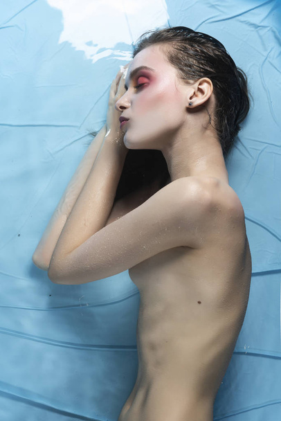 A beautiful naked girl with conceptual makeup in red tones is sl - 写真・画像