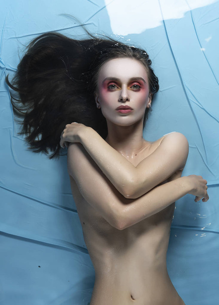 A beautiful naked girl with conceptual makeup in red tones is la - Photo, image