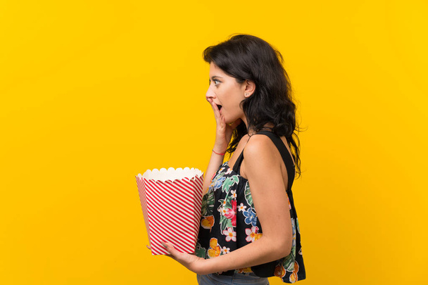 Giovane donna su sfondo giallo isolato con una ciotola di popcorn
 - Foto, immagini