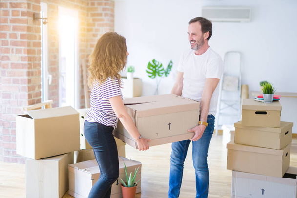 Middle age senior couple moving to a new house, holding cardboard boxing smiling happy in love with apartmant - Photo, Image