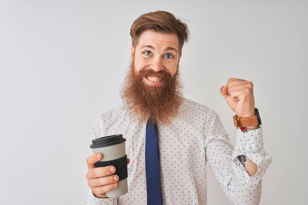 Jonge Redhead Ierse man drinken take-away koffie staande over geïsoleerde witte achtergrond schreeuwen trots en vieren overwinning en succes zeer opgewonden, juichen emotie - Foto, afbeelding