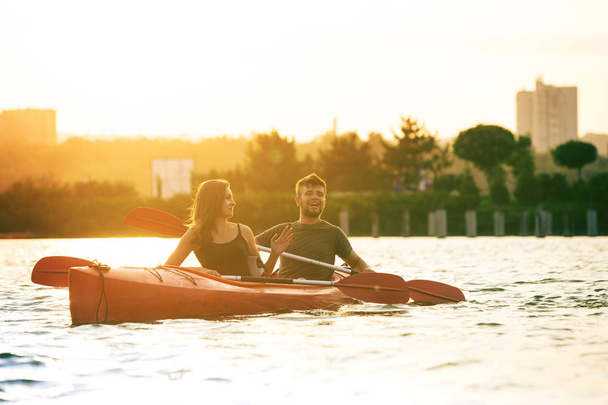 Confident young couple kayaking on river together with sunset on the background - Φωτογραφία, εικόνα