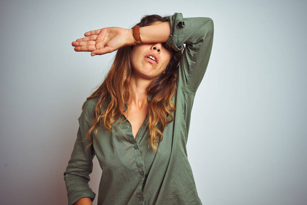 Young beautiful woman wearing green shirt standing over grey isolated background covering eyes with arm, looking serious and sad. Sightless, hiding and rejection concept - Photo, Image