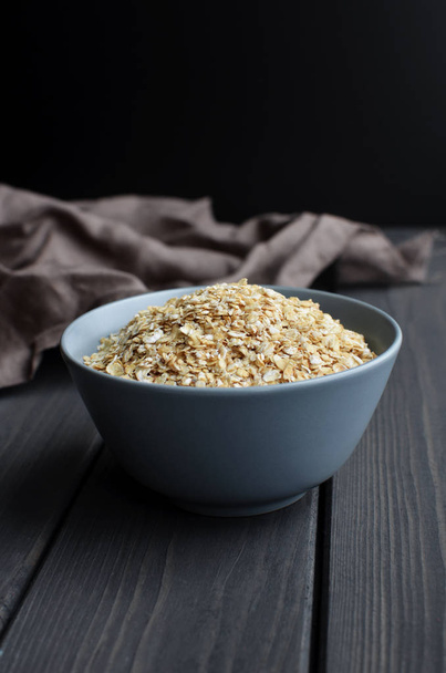 Rolled oats in ceramic bowl on dark wooden table with texture - Foto, immagini