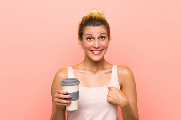 Jeune femme blonde tenant un café à emporter avec expression faciale surprise
 - Photo, image