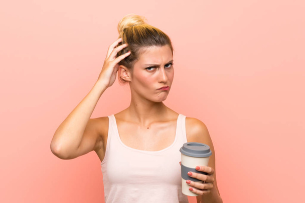 Young blonde woman holding a take away coffee having doubts and with confuse face expression - Foto, imagen