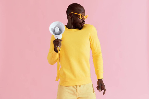 Black man in fashion clothes with megaphone on pink background - Photo, image
