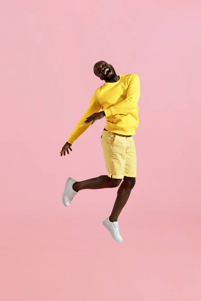 Jump. Happy black man jumping in air laughing on pink background - Φωτογραφία, εικόνα