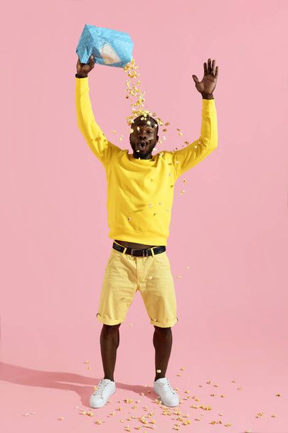 Happy black man having fun pouring pop corn on head in studio - Zdjęcie, obraz