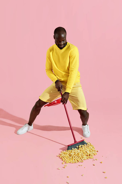 Black man sweeping pop corn on floor on pink background - Fotografie, Obrázek