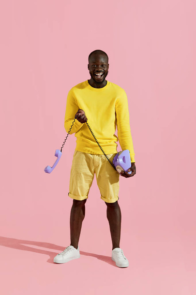 Happy black man in yellow clothes with landline phone on pink  - Zdjęcie, obraz