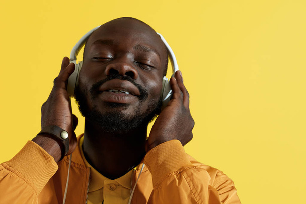 Man in headphones listening music, singing on yellow background - Photo, Image