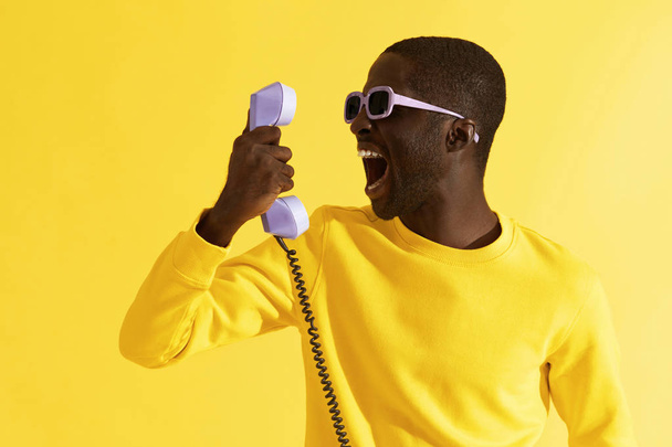 Black man in sunglasses screaming on phone on yellow background - Fotografie, Obrázek