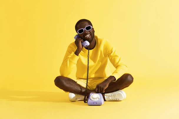 Happy man talking on purple phone sitting on yellow background - Фото, зображення