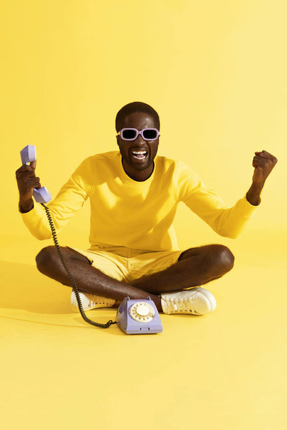 Šťastný vzrušený muž s telefonem oslavující na žlutém pozadí - Fotografie, Obrázek