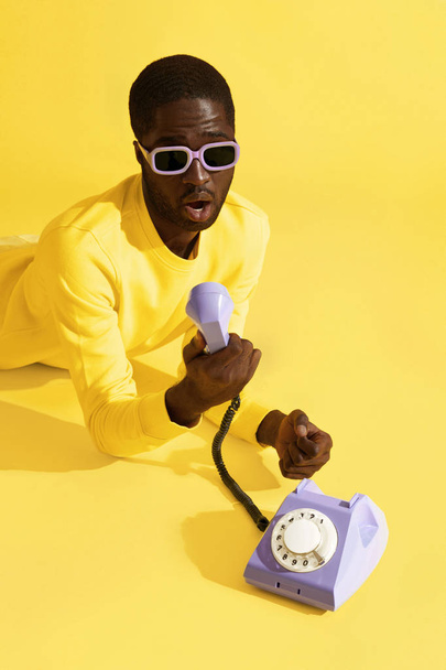 Surprised man in sunglasses with phone on yellow background - Φωτογραφία, εικόνα