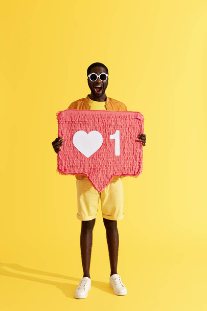 Like. Smiling black man with like icon, heart pinata on yellow - Φωτογραφία, εικόνα
