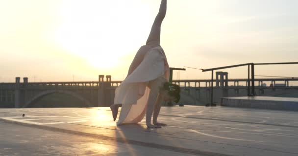 Turnerin macht einen akrobatischen Trick bei Sonnenuntergang. Zwirn in der Luft auf seinen Händen stehend - Filmmaterial, Video