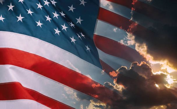 Amerykańska flaga macha w pochmurne niebo i jasny wschód słońca nad horyzontem. - Zdjęcie, obraz