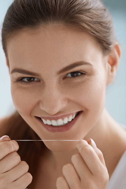 Dental floss. Smiling woman cleaning white teeth with floss - Fotó, kép
