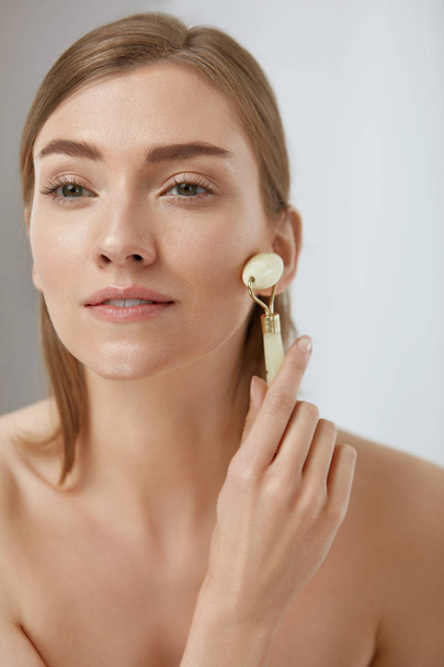 Beauty skin care. Woman using jade roller for face massage - Фото, зображення