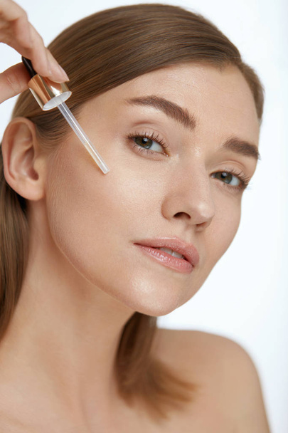 Skin care. Woman applying serum or facial oil on beauty face - Foto, Bild