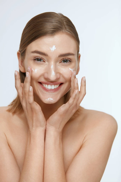 Skin care. Woman applying facial cream on beauty face closeup - Fotó, kép