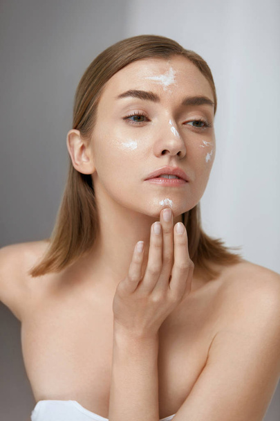 Skin care. Woman applying facial cream on beauty face closeup - 写真・画像