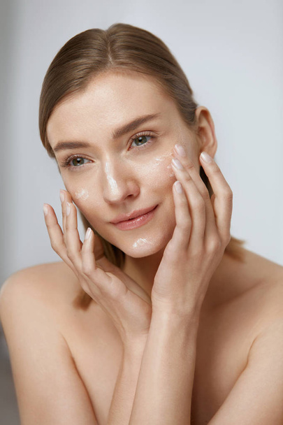 Skin care. Woman applying facial cream on beauty face closeup - Foto, afbeelding