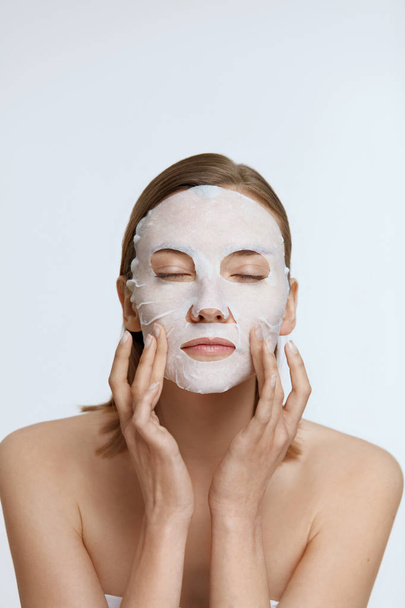 Facial mask. Woman using sheet mask on face skin for spa care - Фото, изображение