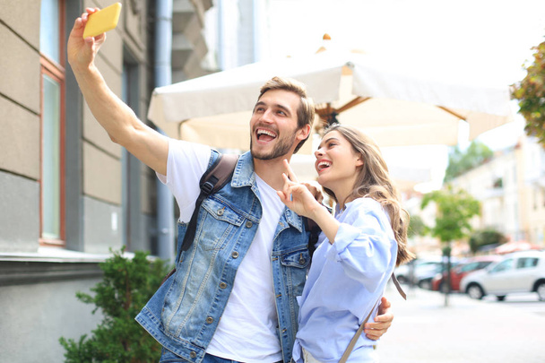 Beautiful lovely young couple walking at the city streets, hugging while taking a selfie. - Valokuva, kuva