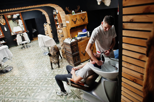Young bearded man washing head by hairdresser while sitting in c - Foto, Bild