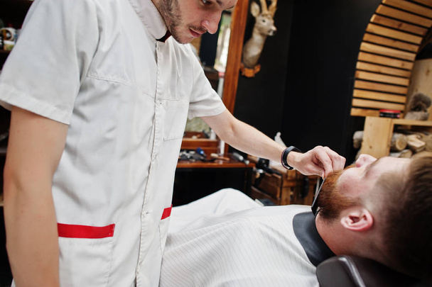 Young bearded man getting haircut by hairdresser while sitting i - Foto, Bild