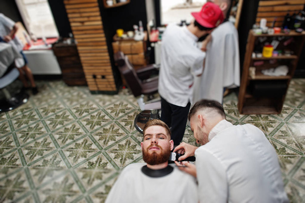 Young bearded man getting haircut by hairdresser while sitting i - Foto, Bild