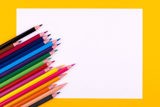 Χρωματιστά αιχμηρά ξύλινα μολύβια βρίσκονται σε ένα λευκό φύλλο χαρτί για δημιουργικότητα, σχέδιο, σημειώσεις, κείμενα και γράμματα - Φωτογραφία, εικόνα