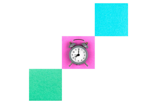 Clock with an alarm clock on a white background lie on colored paper leaves in green, blue and pink for notes - Foto, afbeelding
