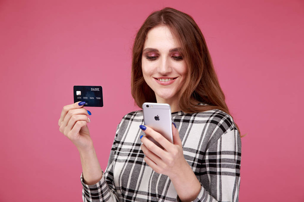 Ευτυχισμένη γυναίκα που κατέχουν πιστωτική κάρτα και το τηλέφωνο στέκεται απομονωμένη στο στούντιο. - Φωτογραφία, εικόνα
