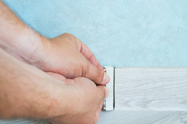 Worker's hands Instal plastic skirting board on laminate flooring. Renovation of baseboard at home. - Photo, Image
