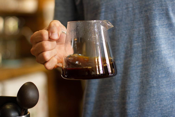 Wide selective closeup shot of a person holding a glass pitcher filled with coffee - 写真・画像