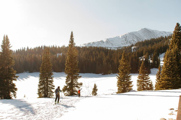 Emberek sétálnak egy havas dombon fák közelében egy havas hegy és egy tiszta ég a háttérben - Fotó, kép